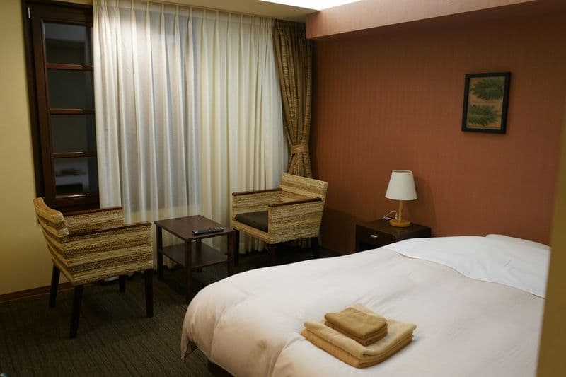 Clean and modest hotel room with a made bed, two rattan armchairs and a small side table — straightforward budget accommodation
