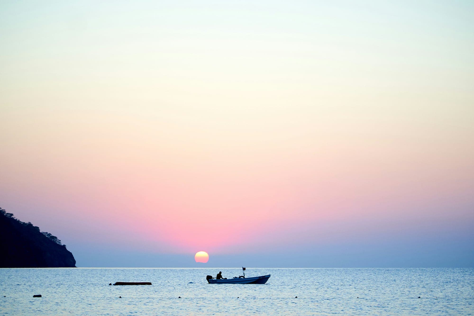 Silhouette of a small boat on calm sea at golden sunset with warm orange reflections on the water