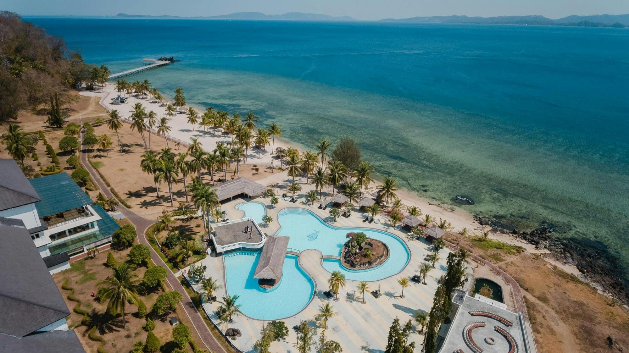 Aerial drone photograph of an Indonesian beachfront resort with pool and palm trees