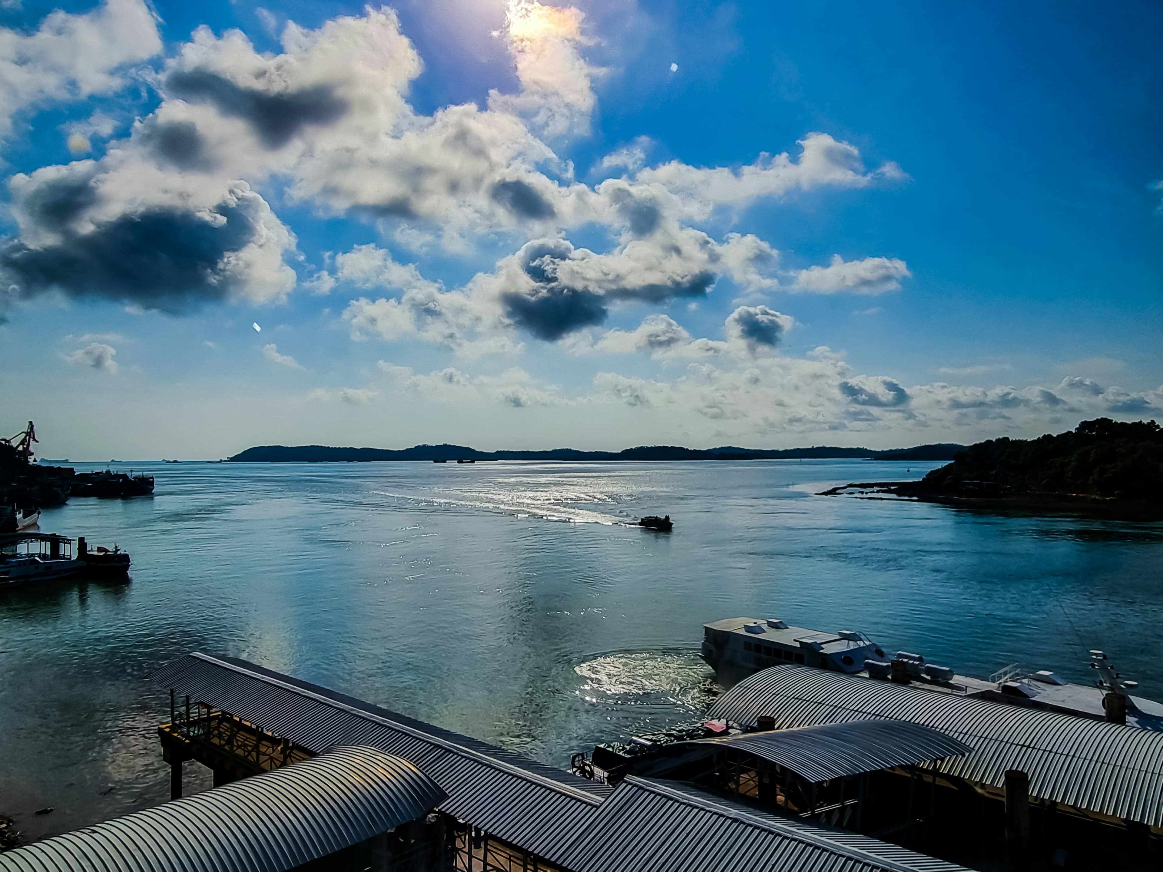 Sunlit Batam waterfront with traditional fishing kelongs and distant islands across calm sea.